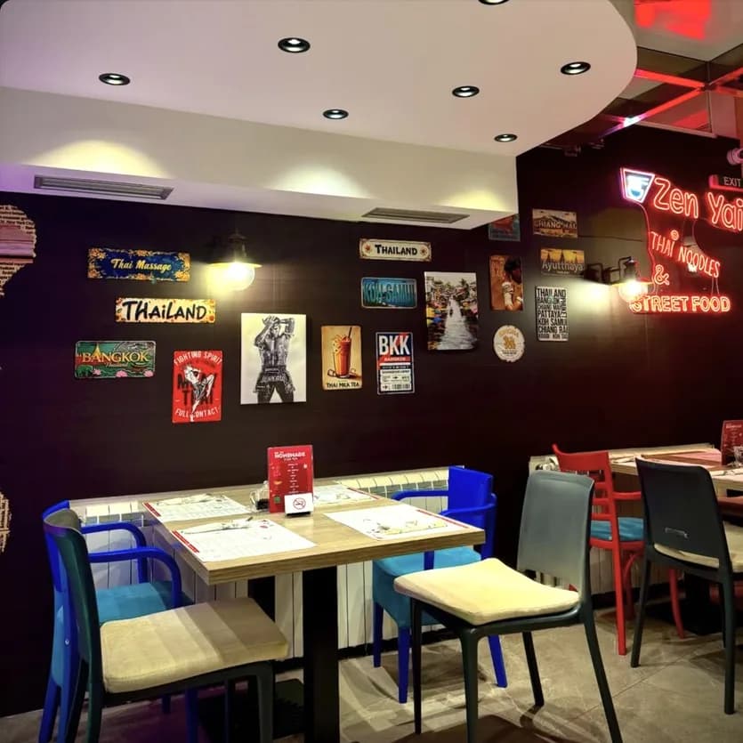 The Zen Yai dining room: a dark wall with Thai signs and posters, the red neon logo, tables and colourful chairs